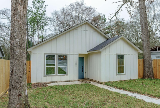 modern inspired farmhouse featuring fence, a front lawn, board and batten siding, and roof with shingles