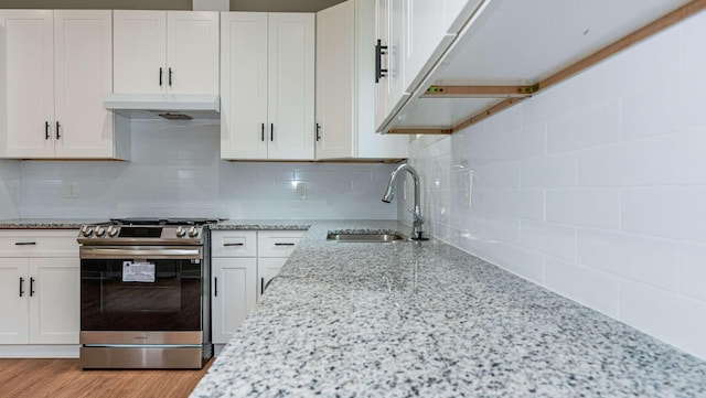 kitchen with light stone counters, stainless steel gas range, under cabinet range hood, white cabinetry, and a sink