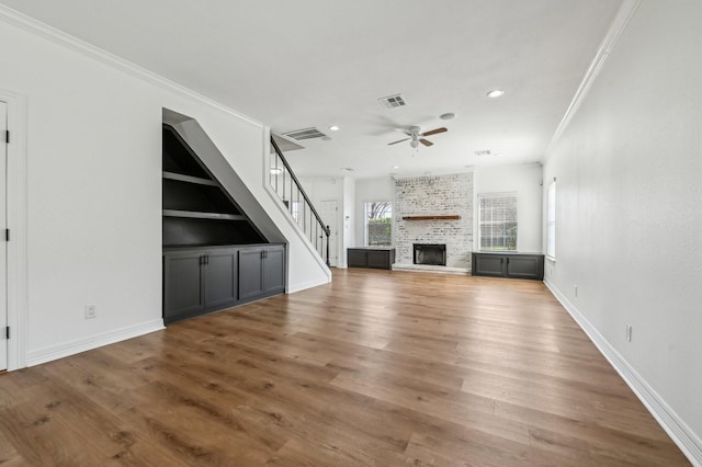 unfurnished living room featuring a large fireplace, visible vents, ceiling fan, wood finished floors, and crown molding