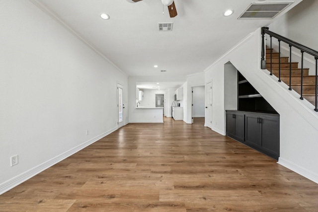 unfurnished living room with stairway, visible vents, crown molding, and wood finished floors