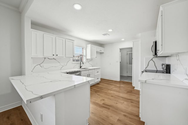 kitchen with a peninsula, a sink, white cabinetry, appliances with stainless steel finishes, and light stone countertops