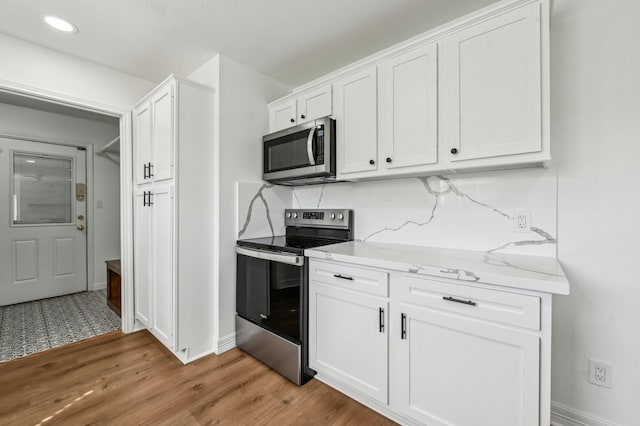 kitchen featuring light wood finished floors, baseboards, appliances with stainless steel finishes, light stone countertops, and white cabinetry