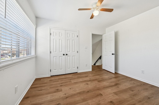 unfurnished bedroom with a closet, wood finished floors, a ceiling fan, and baseboards