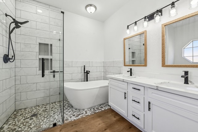 full bathroom featuring wood finished floors, double vanity, a freestanding tub, and a sink