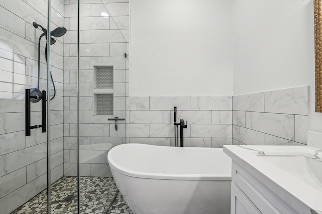 bathroom with a freestanding tub, a shower stall, tile walls, and vanity