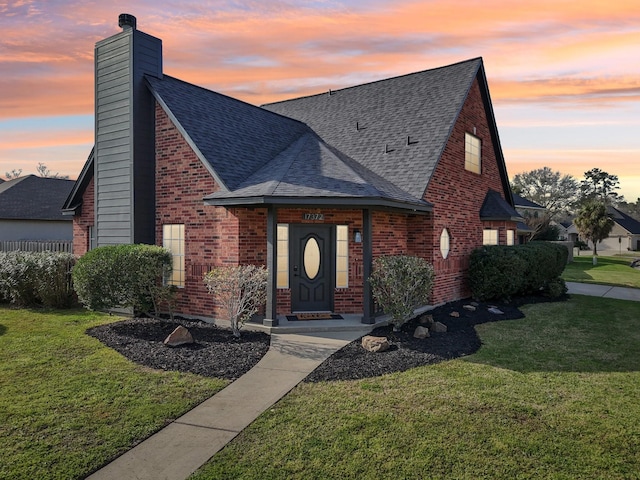 a-frame home featuring a shingled roof, a chimney, a front lawn, and brick siding