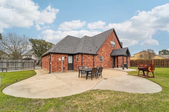 rear view of house with brick siding, a patio, a shingled roof, a lawn, and fence