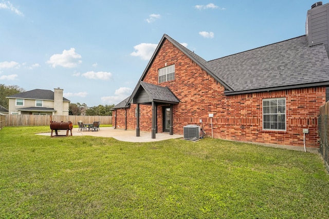 back of property with brick siding, a yard, a shingled roof, fence, and cooling unit