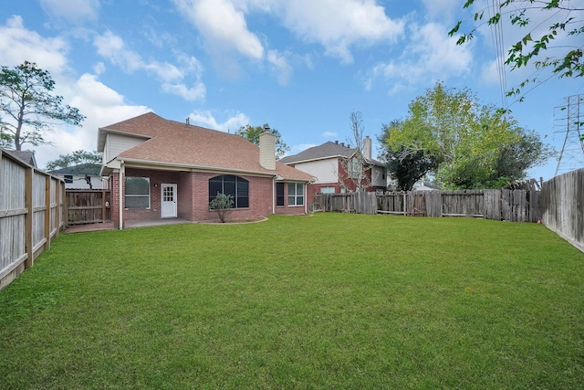 back of property with a fenced backyard, a chimney, roof with shingles, a yard, and brick siding