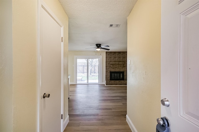 hallway with baseboards, wood finished floors, visible vents, and a textured ceiling