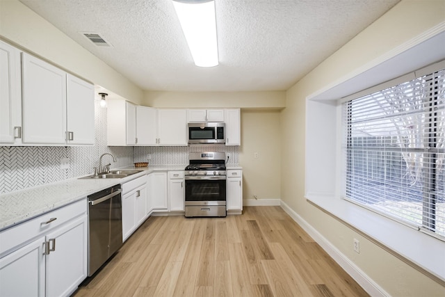 19823 Burle Oak Dr, Humble, TX 77346 - kitchen featuring tasteful backsplash, appliances with stainless steel finishes, light wood-style floors, white cabinetry, and a sink