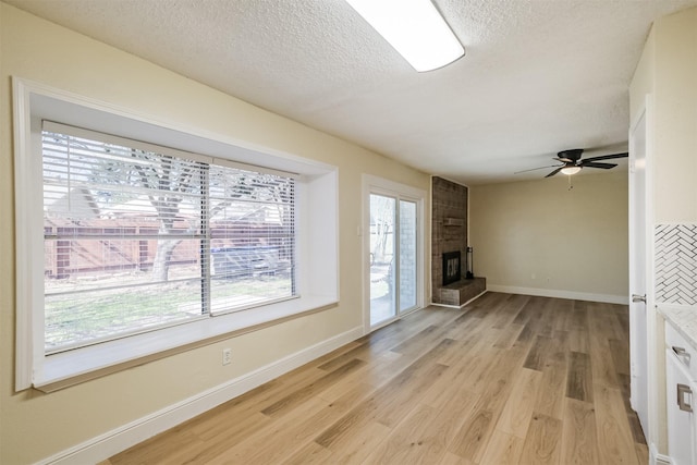 unfurnished living room with light wood finished floors, baseboards, a ceiling fan, a textured ceiling, and a fireplace