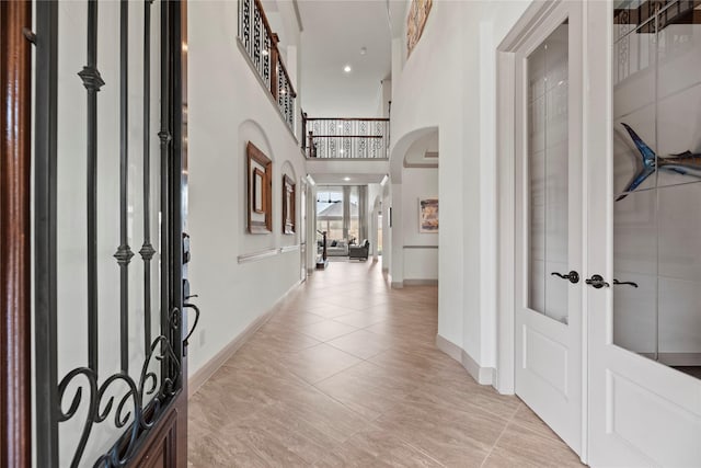 entryway featuring light tile patterned floors, baseboards, arched walkways, a high ceiling, and french doors