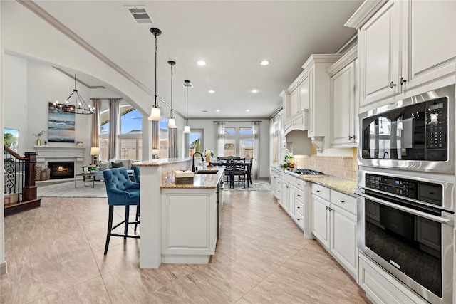 kitchen featuring open floor plan, appliances with stainless steel finishes, an island with sink, and light stone counters