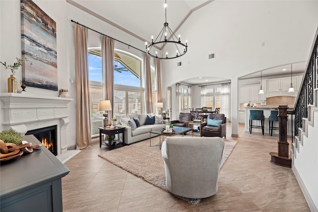 living room featuring visible vents, arched walkways, a premium fireplace, stairway, and a notable chandelier