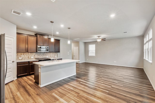 kitchen featuring tasteful backsplash, a center island with sink, hanging light fixtures, stainless steel appliances, and light countertops