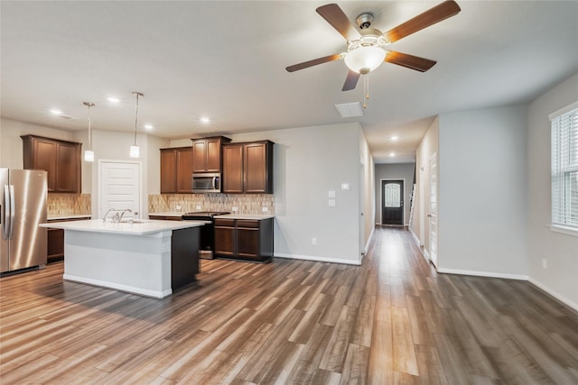 kitchen featuring pendant lighting, a center island with sink, stainless steel appliances, light countertops, and a sink