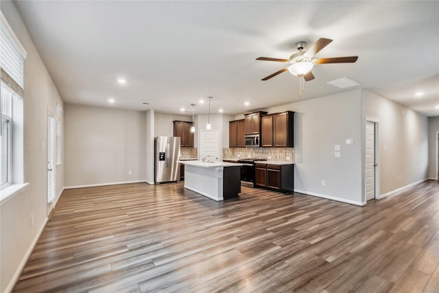 kitchen with stainless steel appliances, open floor plan, light countertops, an island with sink, and decorative light fixtures