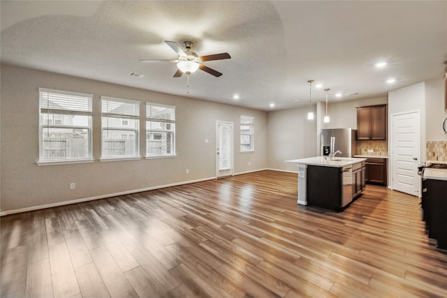 kitchen with light countertops, hanging light fixtures, open floor plan, a kitchen island with sink, and stainless steel fridge