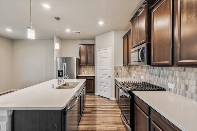 kitchen with stainless steel appliances, a kitchen island with sink, light countertops, and a sink