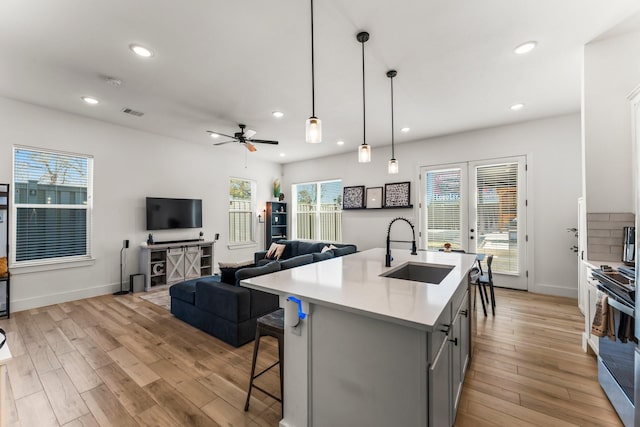 kitchen featuring pendant lighting, light countertops, gray cabinetry, open floor plan, and a sink