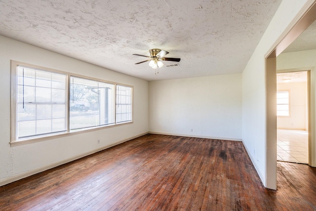 empty room featuring ceiling fan, visible vents, dark wood finished floors, and a textured ceiling