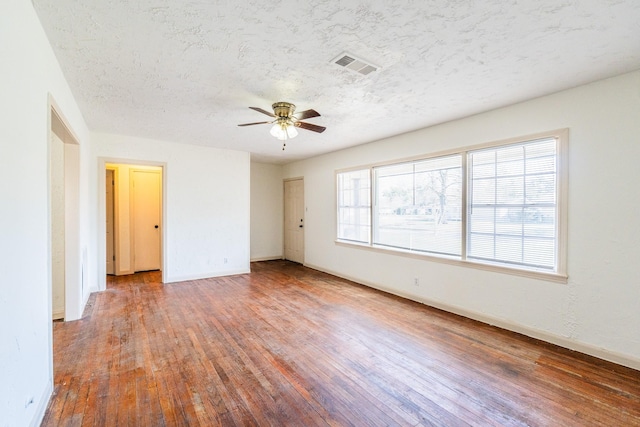 empty room featuring visible vents, a ceiling fan, a textured ceiling, wood finished floors, and baseboards