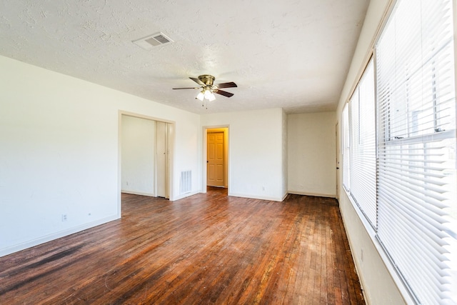 unfurnished bedroom with a textured ceiling, dark wood-style flooring, visible vents, and baseboards