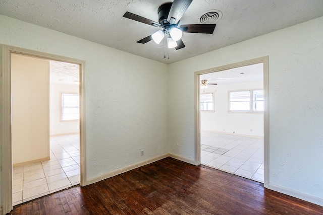 empty room with a textured wall, plenty of natural light, wood finished floors, and visible vents