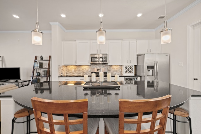 kitchen with a center island with sink, dark countertops, decorative light fixtures, stainless steel appliances, and white cabinetry