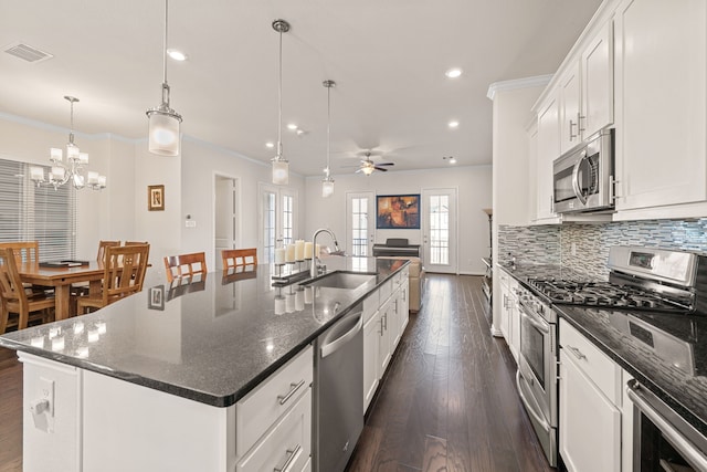 kitchen with a center island with sink, white cabinets, hanging light fixtures, stainless steel appliances, and a sink