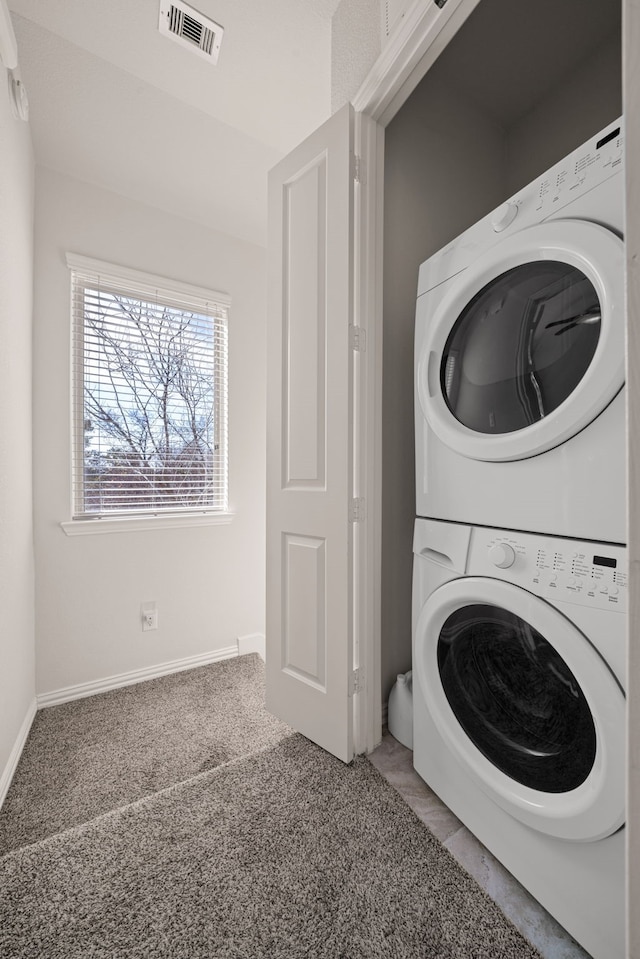 clothes washing area with laundry area, baseboards, visible vents, carpet, and stacked washing maching and dryer