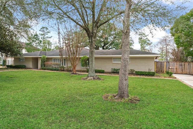 ranch-style home featuring brick siding, fence, and a front lawn