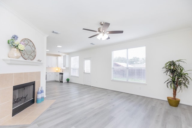 living room featuring light wood-type flooring, ornamental molding, a fireplace, and visible vents