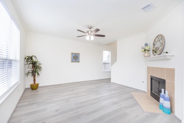 living area featuring crown molding, visible vents, light wood-style floors, ceiling fan, and a tile fireplace