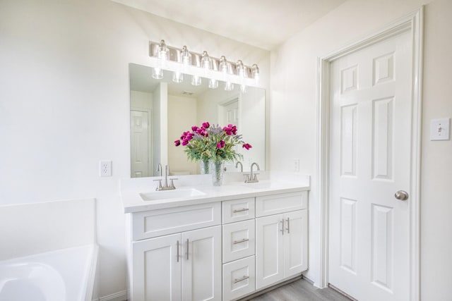 full bath featuring double vanity, a tub to relax in, a sink, and wood finished floors