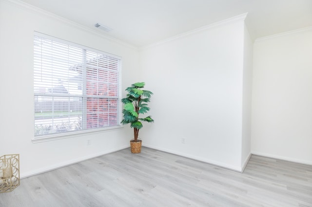 empty room featuring light wood-style flooring, visible vents, ornamental molding, and baseboards