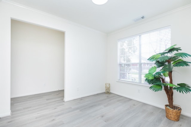 empty room with light wood-type flooring, visible vents, crown molding, and baseboards