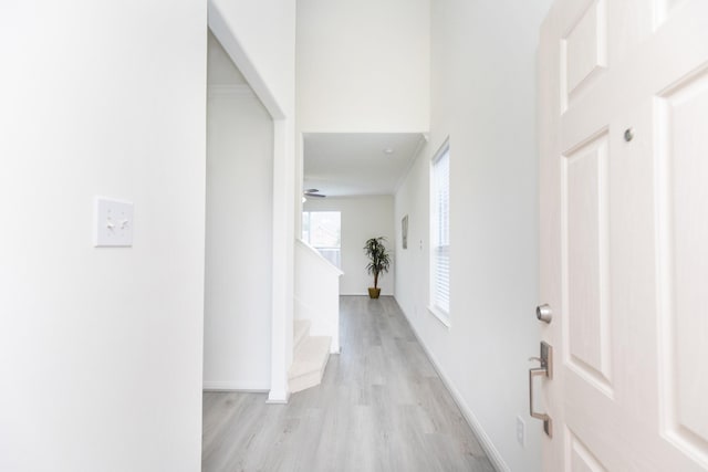 hall featuring light wood finished floors, baseboards, and stairway