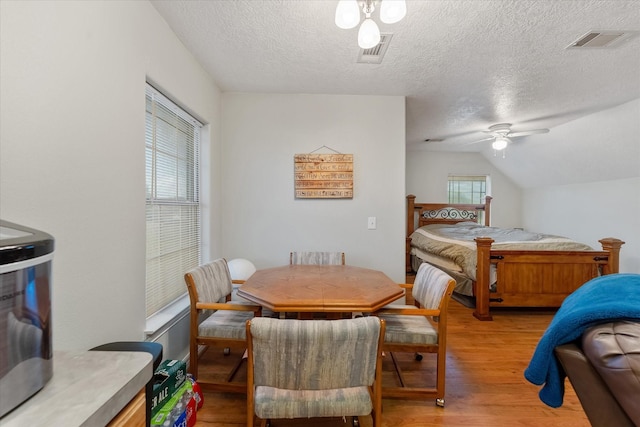 bedroom featuring light wood-style floors, visible vents, vaulted ceiling, and a textured ceiling