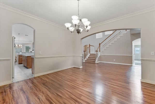 interior space with crown molding, arched walkways, light wood finished floors, and a notable chandelier