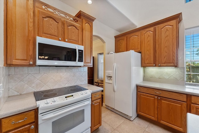 kitchen with white appliances, light countertops, brown cabinets, tasteful backsplash, and arched walkways