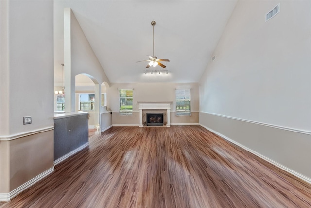 unfurnished living room featuring visible vents, wood finished floors, high vaulted ceiling, a fireplace with flush hearth, and ceiling fan with notable chandelier