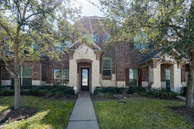 view of front facade featuring stone siding, a front yard, and brick siding