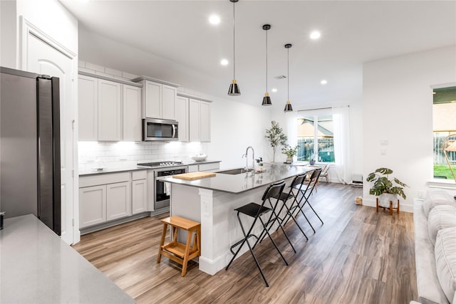 kitchen featuring decorative light fixtures, tasteful backsplash, appliances with stainless steel finishes, a kitchen island with sink, and a kitchen breakfast bar