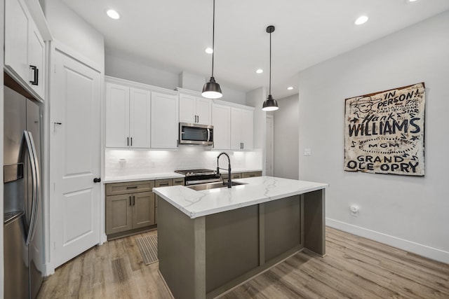 kitchen featuring light stone counters, a center island with sink, hanging light fixtures, appliances with stainless steel finishes, and white cabinetry