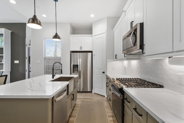 kitchen with light stone counters, decorative light fixtures, a center island with sink, appliances with stainless steel finishes, and white cabinets