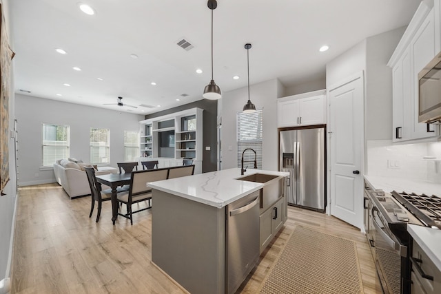 kitchen featuring pendant lighting, appliances with stainless steel finishes, open floor plan, a kitchen island with sink, and white cabinetry