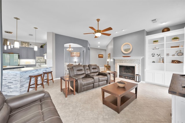 living room featuring light tile patterned floors, visible vents, arched walkways, ceiling fan, and a fireplace