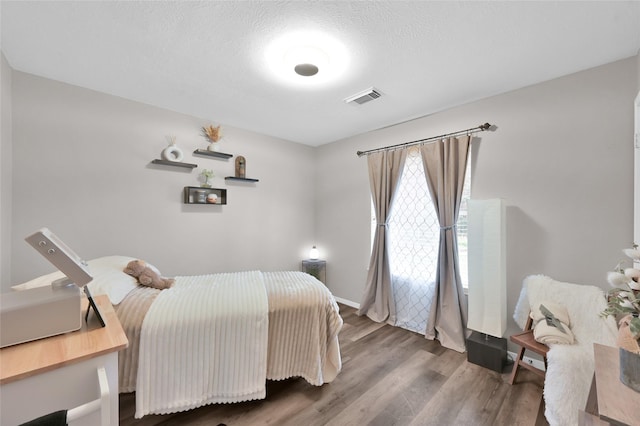 bedroom featuring a textured ceiling, wood finished floors, visible vents, and baseboards